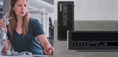 Eine junge Frau betrachtet konzentriert eine feingliedrige mechanische Greifarm-Konstruktion aus Metall, während daneben die Vorder- und Rückansicht einer kompakten Lenovo ThinkStation mit verschiedenen Anschlüssen abgebildet ist.