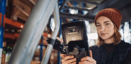 Das Bild zeigt CORE-Z5 ist das erste 5G-Smartphone des französischen Herstellers Crosscall, das speziell für kritische Umgebungen entwickelt wurde. Das Gerät ist in Anwendung in rauher Werkstattumgebung, gehalten von einer jungen Frau bei der Arbeit.