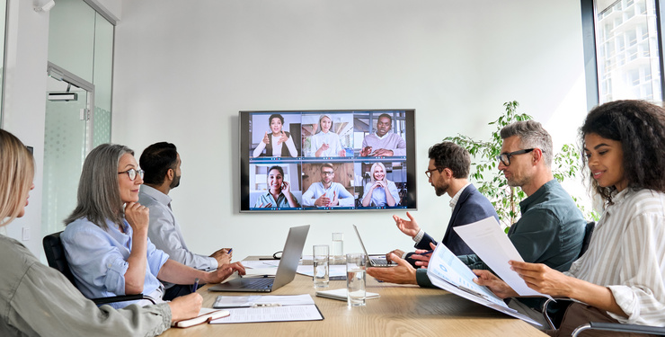 Mehrere Personen sitzen in einem Konferenzraum und nehmen an einer Videokonferenz teil.