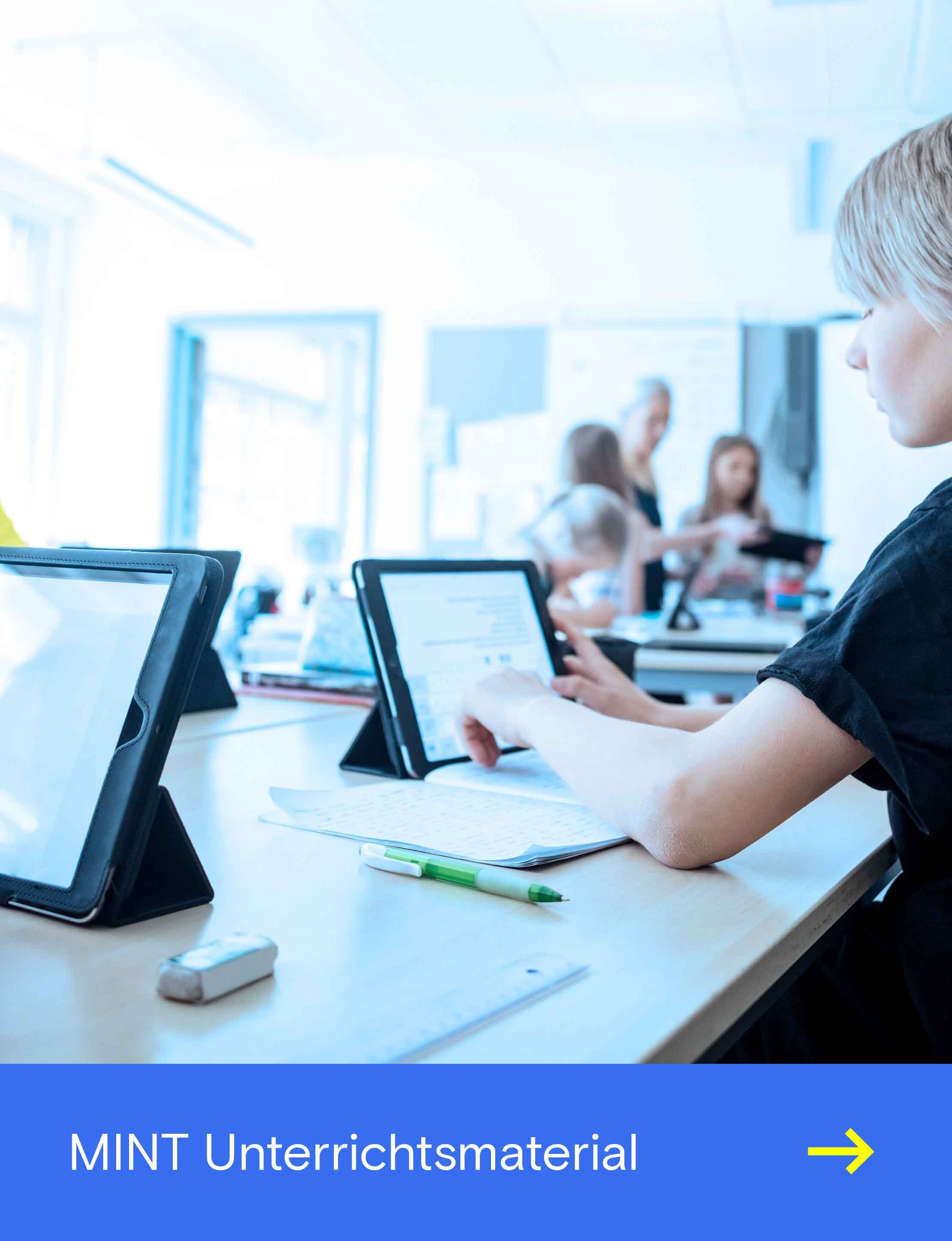 Mehrere Personen arbeiten in einem hellen Raum an Tablets mit Tastatur und Stift auf einem gemeinsamen Tisch.