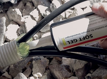 Ein Arbeiter appliziert mit einer Kartusche grünes Isoliergel in ein Wellrohr, um die darin verlaufenden elektrischen Kabel gegen Feuchtigkeit abzudichten.