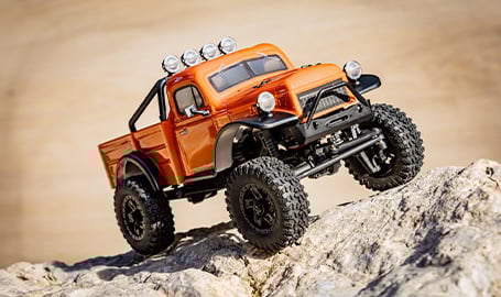 Sechs verschiedene Modelle des ferngesteuerten Autos "Hobby Plus EVO Crawler V2", die auf dem felsigen Ufer eines Flusses aufgereiht sind.