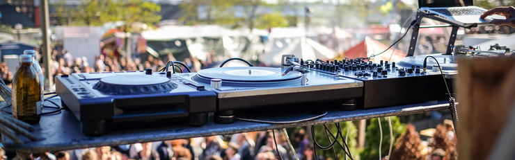 DJ-Equipment auf einer Bühne mit unscharfem Festivalpublikum im Hintergrund