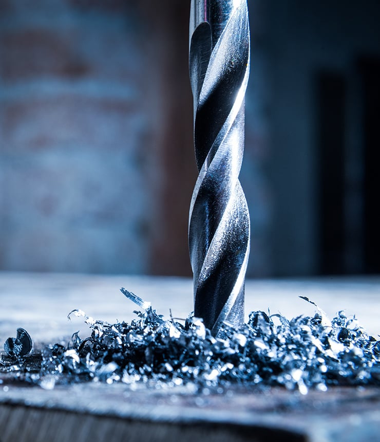 Ein Metallbohrer bohrt in eine Metalloberfläche, wobei Metallspäne entstehen.
