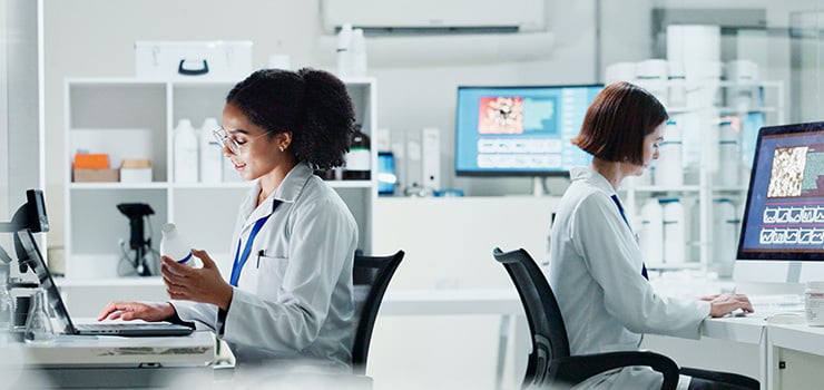 Zwei Wissenschaftlerinnen in weißen Kitteln arbeiten im modernen Labor an Computern