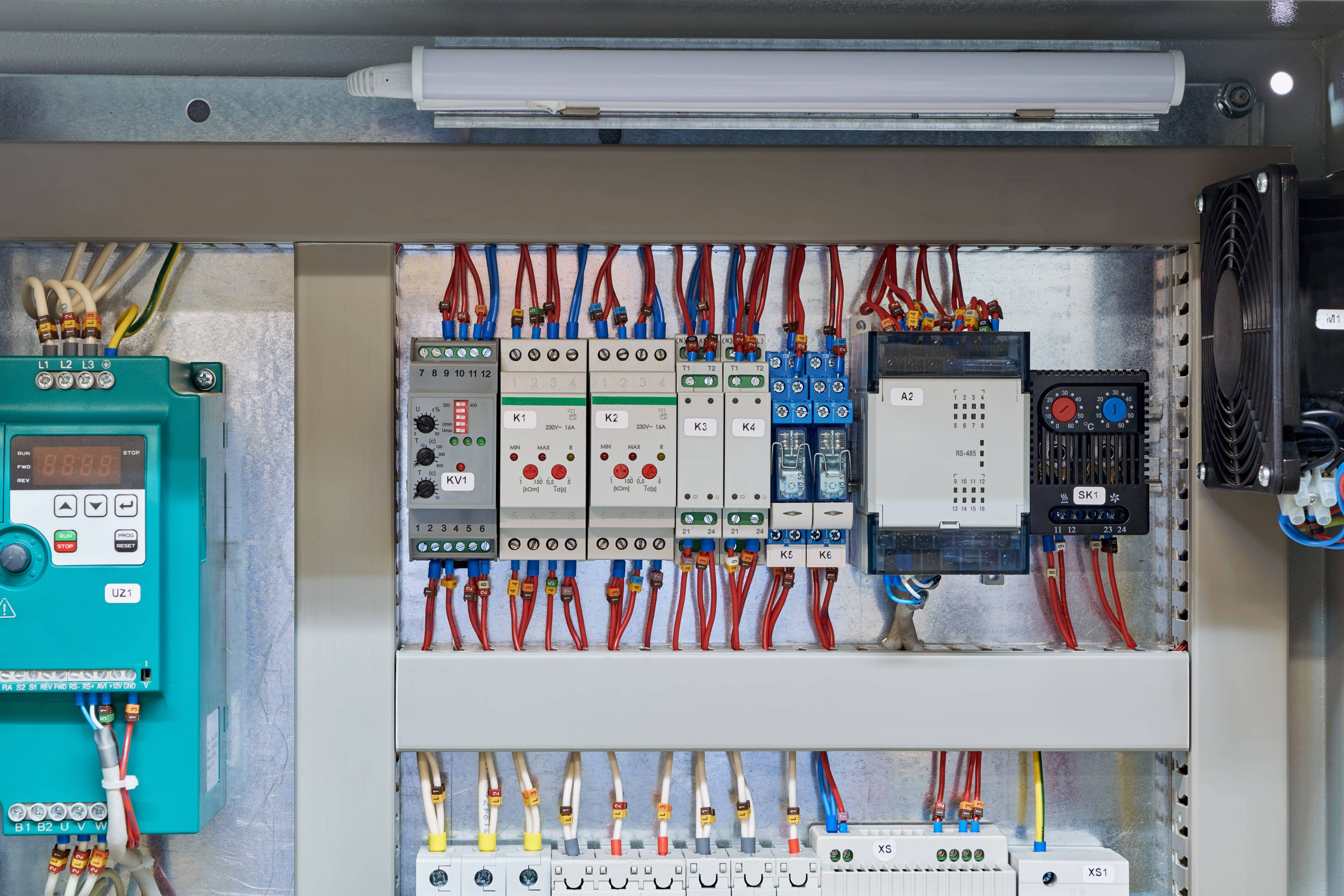 Elektrischer Schaltschrank mit verschiedenen Steuerungs- und Schutzgeräten, verbunden durch rote und blaue Kabel.