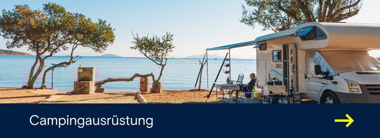 Ein Wohnmobil steht auf einem Campingplatz direkt am Meer, mit Markise, Stühlen und Blick auf das Wasser.