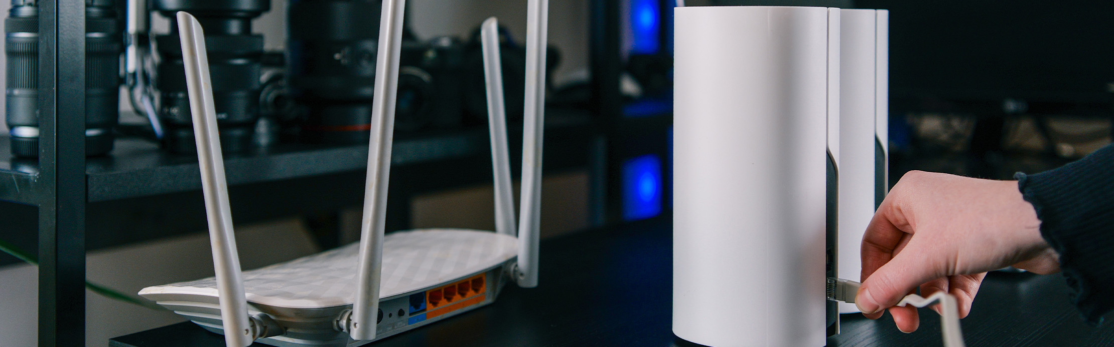 Person verbindet ein Netzwerkkabel mit einem Router neben einem WLAN-Router mit Antennen