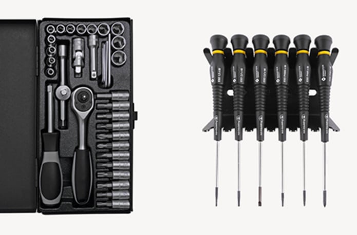 Ein geöffneter, schwarzer Steckschlüsselsatz mit Knarre und Bits auf der linken Seite sowie ein sechsteiliges Elektronik-Schraubendreher-Set in einem Ständer auf der rechten Seite vor weißem Hintergrund.