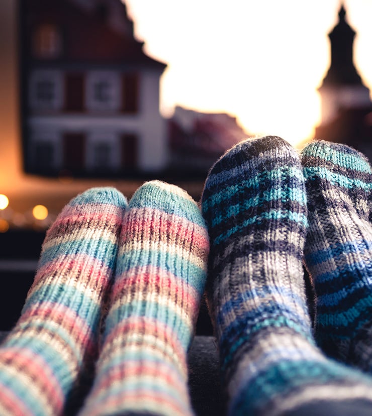 Nahaufnahme von zwei Paar Füßen in gestrickten, bunten Socken, im unscharfen Hintergrund.