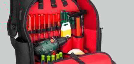 Ein schwarzer Werkzeugrucksack mit rotem Innenfutter, in dem verschiedene Werkzeuge wie Schraubendreher, ein Hammer und ein Akkubohrer ordentlich in elastischen Schlaufen und Taschen verstaut sind.