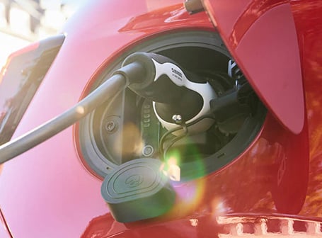 Ein weißer Stecker ist in die Ladebuchse eines roten Elektroautos gesteckt, um es aufzuladen.