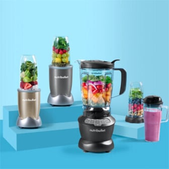 Das Bild zeigt eine Gruppe von NutriBullet Mixern in verschiedenen Größen und Farben, einige mit klaren Behältern gefüllt mit bunten Früchten und Gemüse, auf hellblauen, stufenförmigen Podesten vor einem hellblauen Hintergrund.