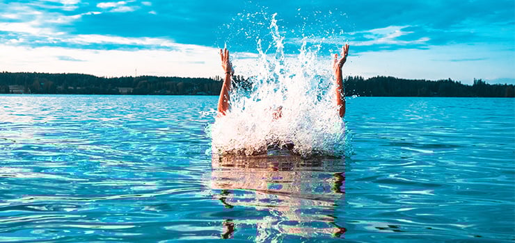 Person ist mit hochgeworfenen Armen ins Wasser gesprungen.