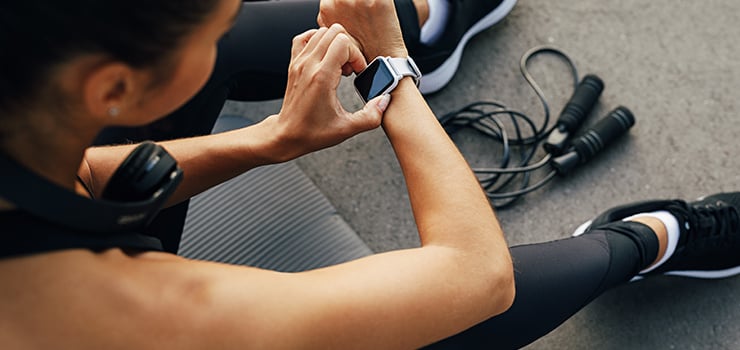 Person beim Training überprüft eine Smartwatch, Fitness-Tracker am Handgelenk, Springseil und Sportbekleidung – Aktivitäts- und Trainingskontrolle im Alltag.