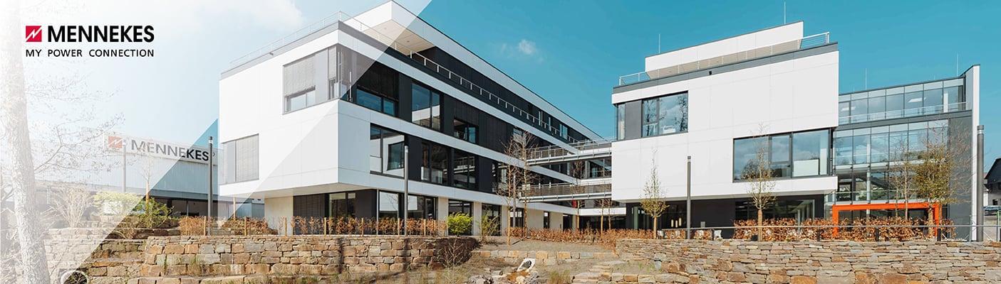  Ein großes, modernes Bürogebäude aus weißem Beton und Glas, mit einem Innenhof und Steinmauern im Vordergrund, unter einem klaren blauen Himmel.