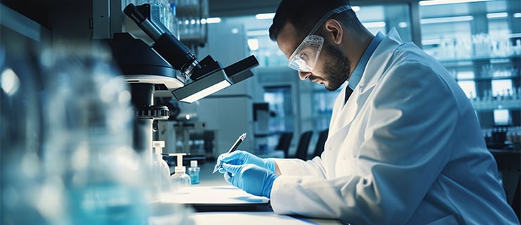 Wissenschaftler mit Schutzbrille und Handschuhen arbeitet am Mikroskop - Laborsicherheit