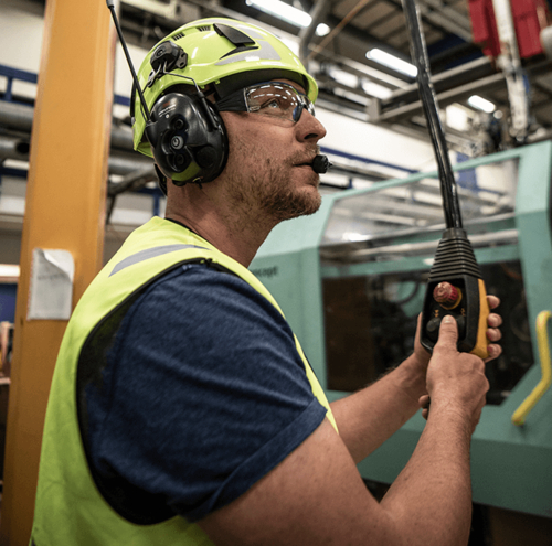 Mann trägt 3M™ PELTOR™ WS™ LiteCom Plus Headset, Schutzhelm und Warnweste; bedient Steuerung in Industrie.