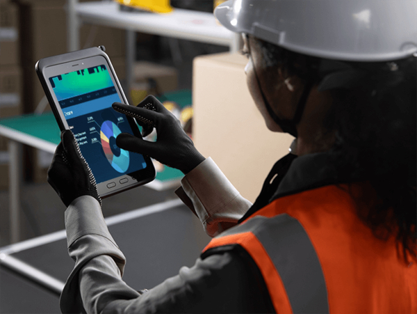 Person mit Schutzhelm und Warnweste bedient robustes Tablet mit Datencharts in Industrieumgebung.