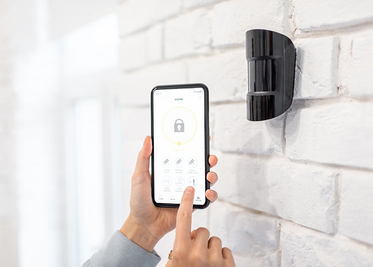 Smartphone steuert einen Bewegungsmelder oder ein Sicherheitssystem an einer Hauswand.