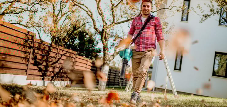Ein Mann verwendet einen Laubbläser, um heruntergefallene Herbstblätter in seinem Garten aufzusammeln.