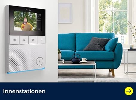 Eine weiße Innenstation einer Türsprechanlage ist an einer Wand montiert, auf deren Bildschirm ein Paketbote mit einem Karton zu sehen ist, während im Hintergrund ein Wohnzimmer mit einem türkisfarbenen Sofa abgebildet ist.
