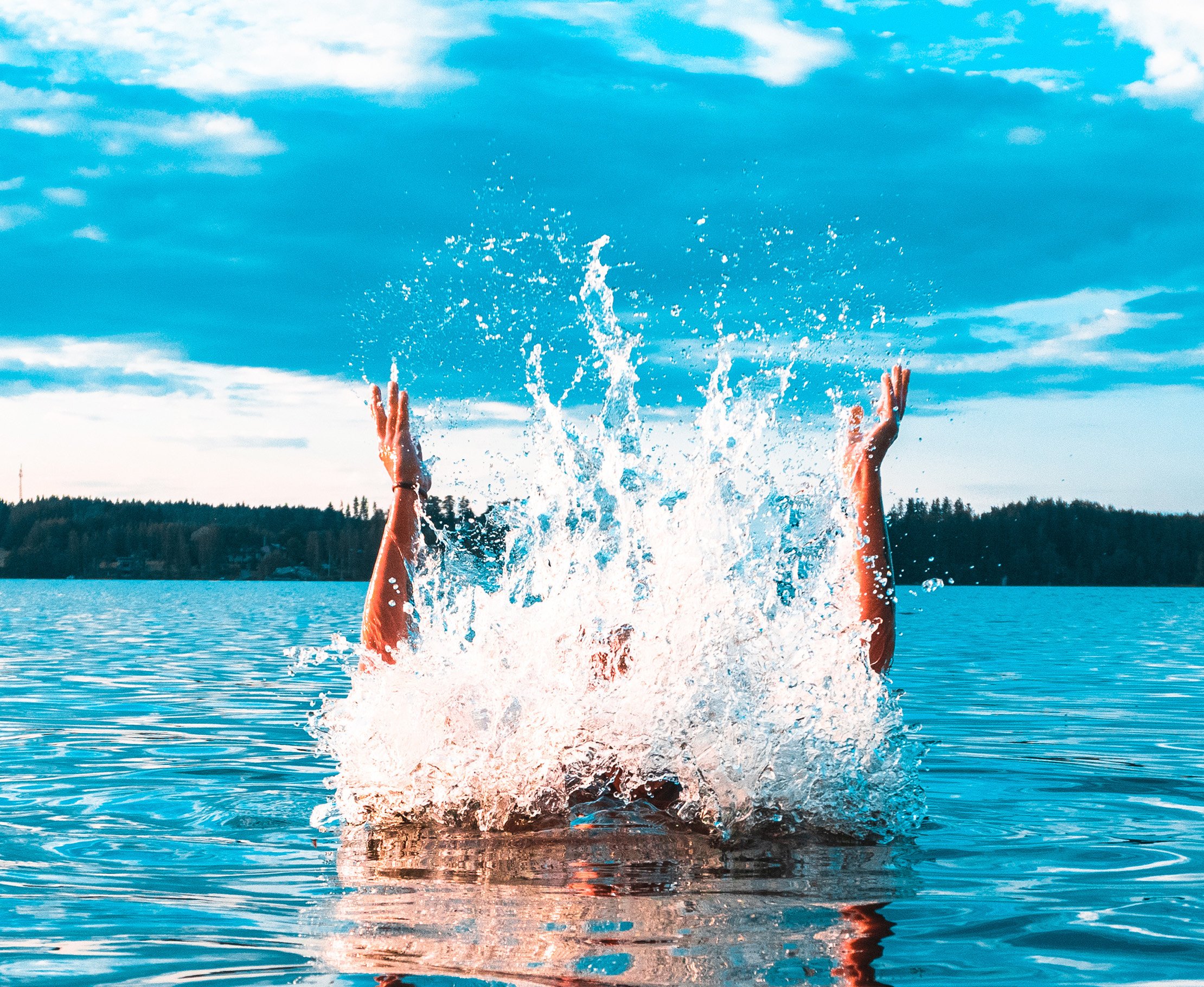 Eine Person springt mit ausgestreckten Armen aus einem See