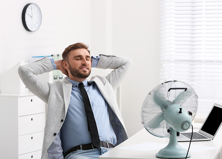 Ein Mann im Anzug sitzt im Büro entspannt vor einem Tischventilator.
