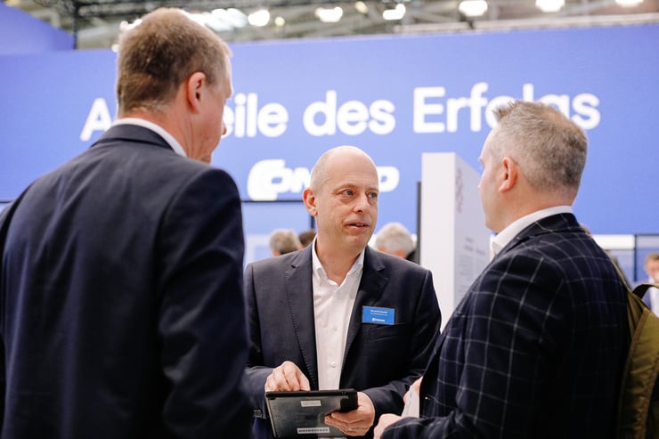Drei Personen stehen vor einer blauen Wand mit der Aufschrift Alle Teile des Erfolgs