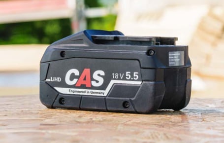 Ein schwarzer Cordless Alliance System LiHD-Wechselakku mit der Aufschrift „CAS 18V 5.5“ liegt auf einer Holzoberfläche.