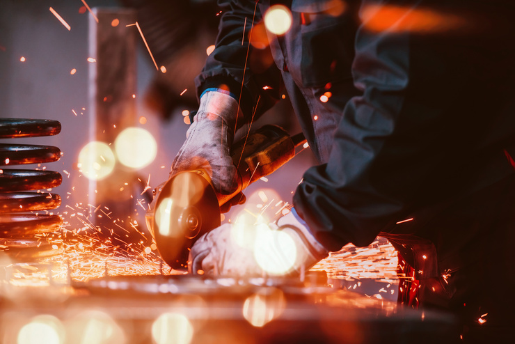 Ein Arbeiter schneidet Metall mit einer elektrischen Trennscheibe, wobei Funken fliegen.