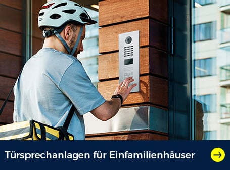  Ein Mann mit einem Fahrradhelm und einer gelben Liefertasche drückt auf die Klingel einer modernen Türsprechanlage an einem Gebäude mit Holz- und Glasfassade.