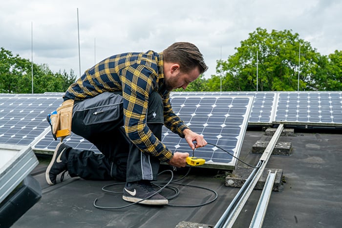 Techniker kniet auf Dach und wartet Solarpanels mit Weicon Abisolierzange.