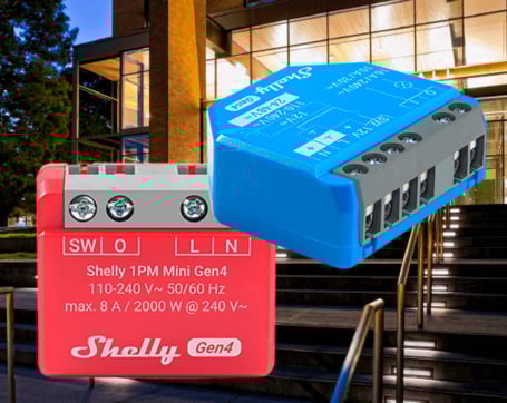 Zwei Shelly Gen4 Smart-Home-Module, ein rotes 1PM Mini und ein blaues, schweben vor dem beleuchteten Eingang eines modernen Gebäudes.