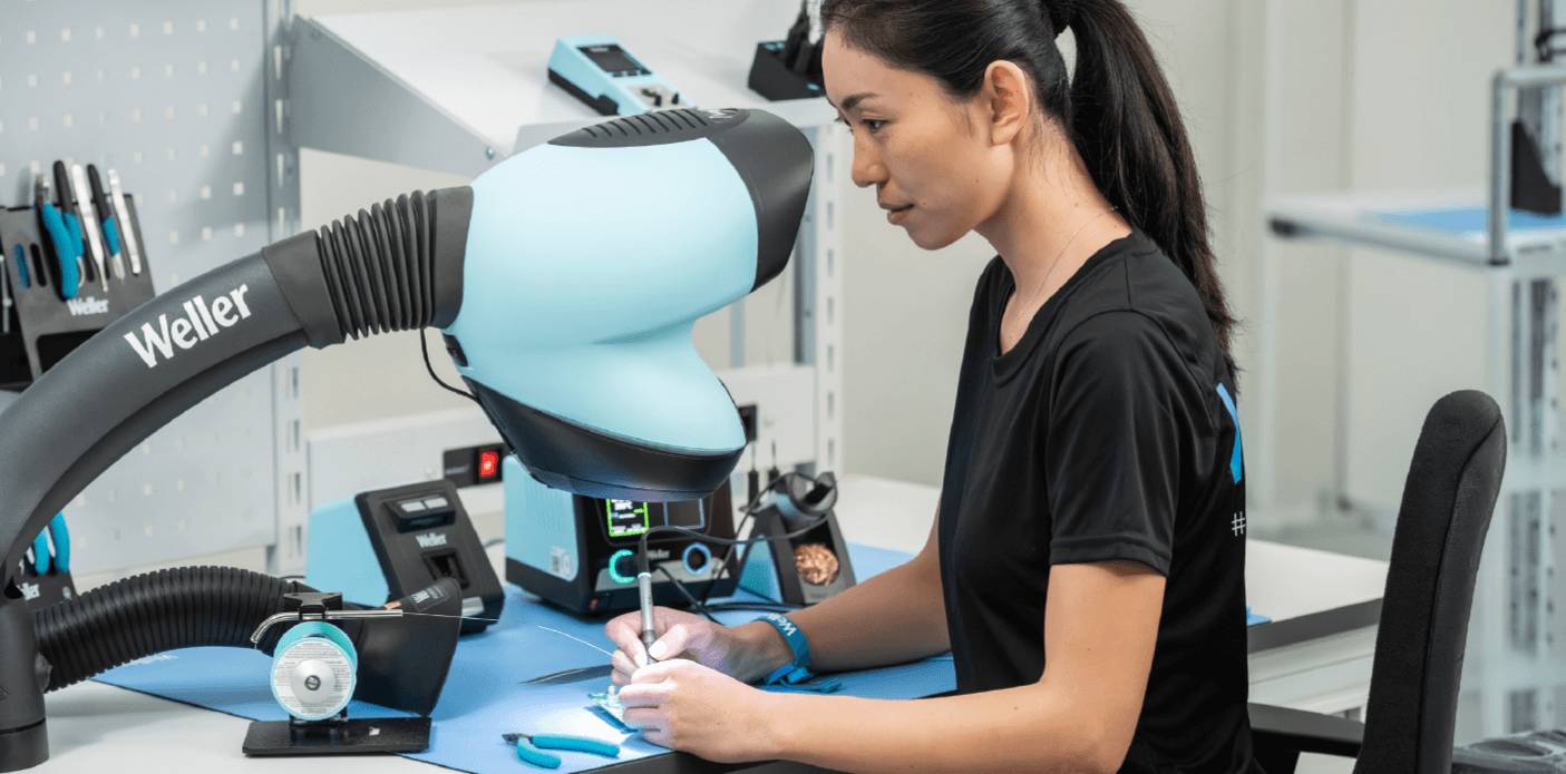 Eine Technikerin arbeitet an einem Elektronikarbeitsplatz unter einer Lötrauchabsaugung der Marke Weller.