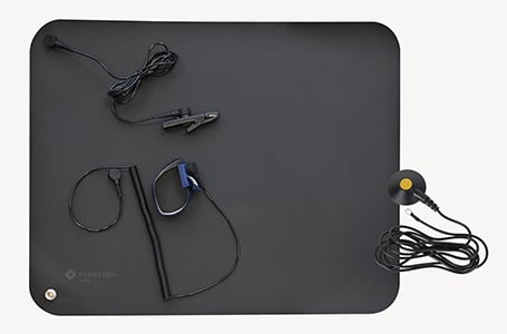 Eine schwarze ESD-Arbeitsplatzmatte von Bernstein in der Draufsicht, ausgestattet mit einem Erdungskabel inklusive Krokodilklemme, einem blauen ESD-Armband mit Spiralkabel und einem gelb-schwarzen Erdungsbaustein.