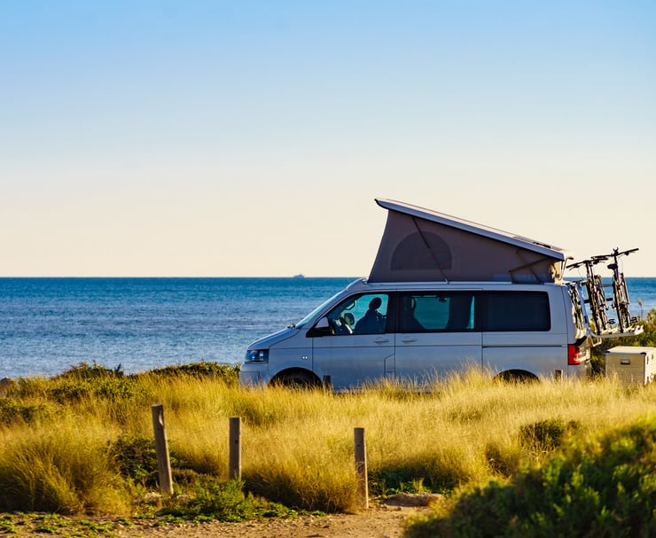  Ein Campingbus mit ausgeklapptem Dach steht am Meer, im Hintergrund ist der Horizont sichtbar.