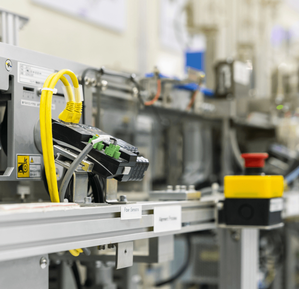 Industrielle Anlage mit gelben Kabeln, Elektronikkomponenten und einem roten Not-Aus-Schalter im Fokus.