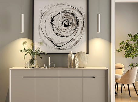  Eine elegante Kommode in einer Wohnung, dekoriert mit Vasen und Kerzen, darüber ein großformatiges, abstraktes Kunstwerk, das von zwei zylindrischen 1-Phasen-Schienensystem-Pendelleuchten beleuchtet wird.