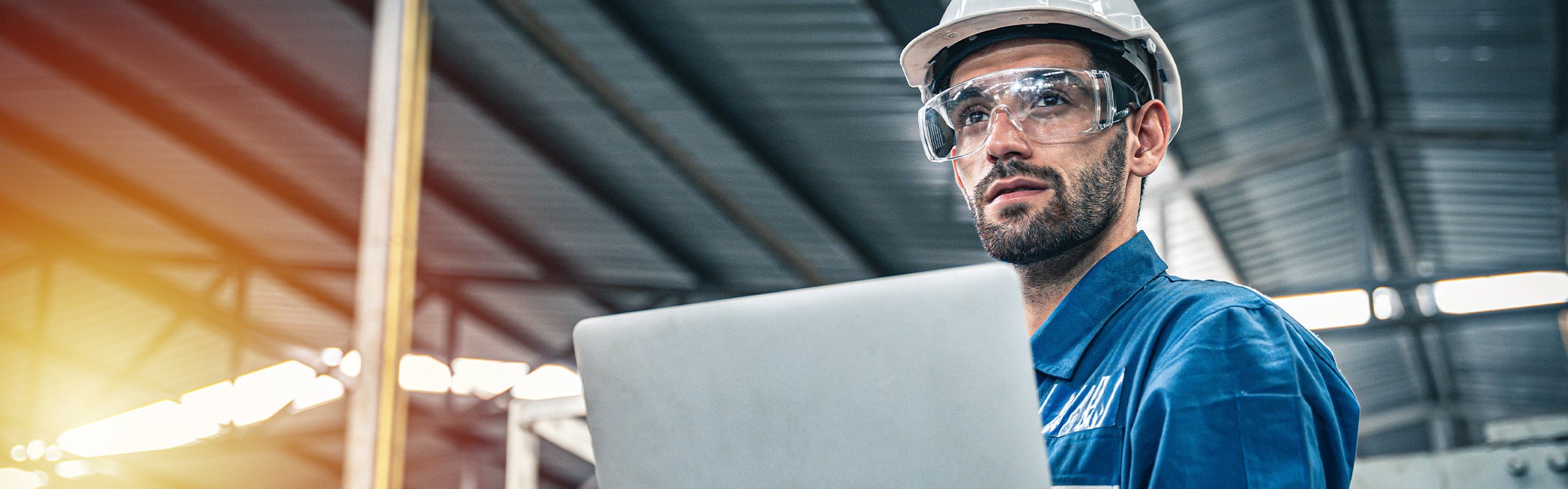 Techniker mit Schutzhelm und Schutzbrille arbeitet mit einem Laptop in einer Industriehalle