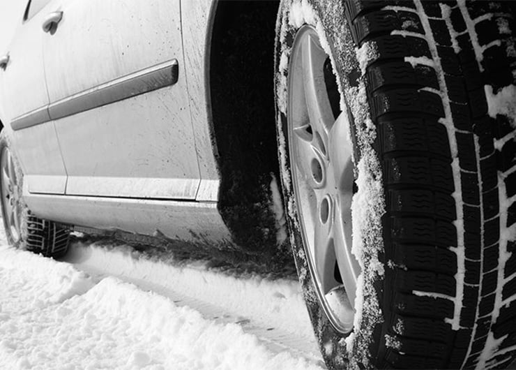 Ein Graues Auto Nahaufnahme von vorne unten im Schnee. Auf dem Reifen ist auch Schnee ersichtlich.