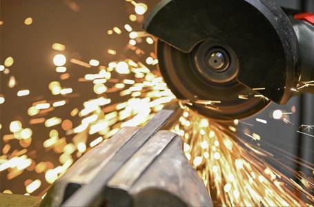 Ein Winkelschleifer schneidet ein in einem Schraubstock eingespanntes Metallstück, wobei ein intensiver Funkenflug entsteht.