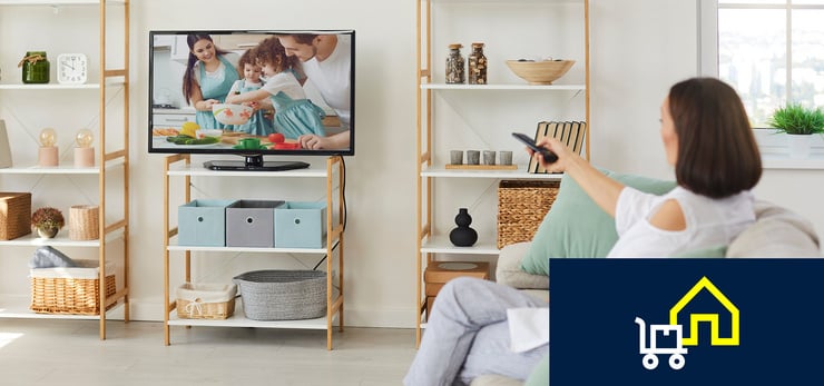 Person sitzt auf dem Sofa und steuert mit einer Fernbedienung den Fernseher im Wohnzimmer.
