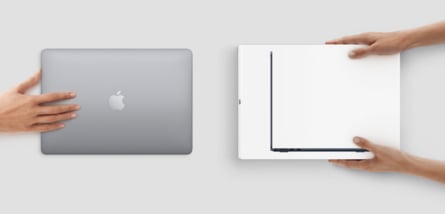 Zwei Hände halten ein geschlossenes graues Apple MacBook mit dem Apfel-Logo, während zwei weitere Hände ein dünneres, weißes Notebook von der Seite halten, um die Dicke zu vergleichen.