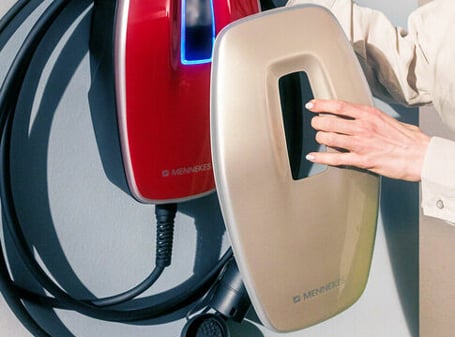 Eine weibliche Hand hält eine goldene Abdeckung für eine rote Wallbox.