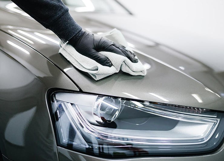 Eine Nahaufnahme eines Dunkelgrauen Autos welches gerade poliert wird mit einem weissen Lappen.