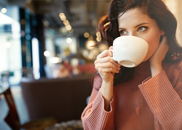 Eine Frau sitzt in einem Kaffee und trinkt aus einer grossen weissen Tasse.