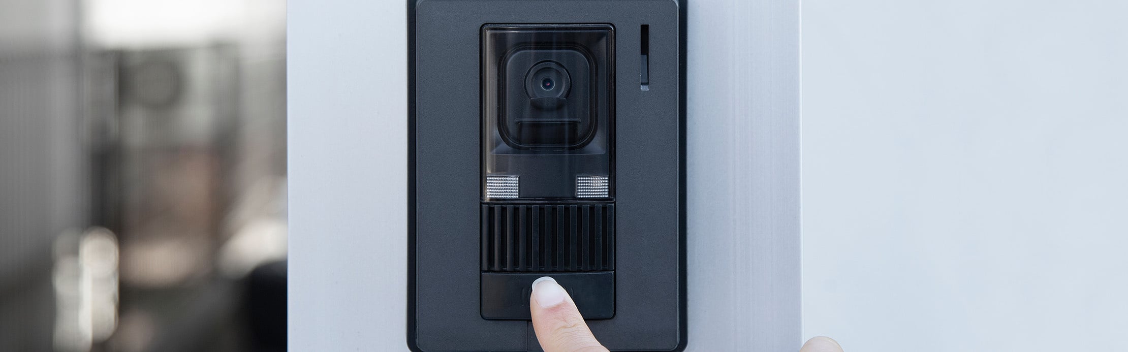 Smarte Video-Türsprechanlage mit integrierter Kamera an einer Hauseingangssäule, während eine Person die Klingel betätigt.