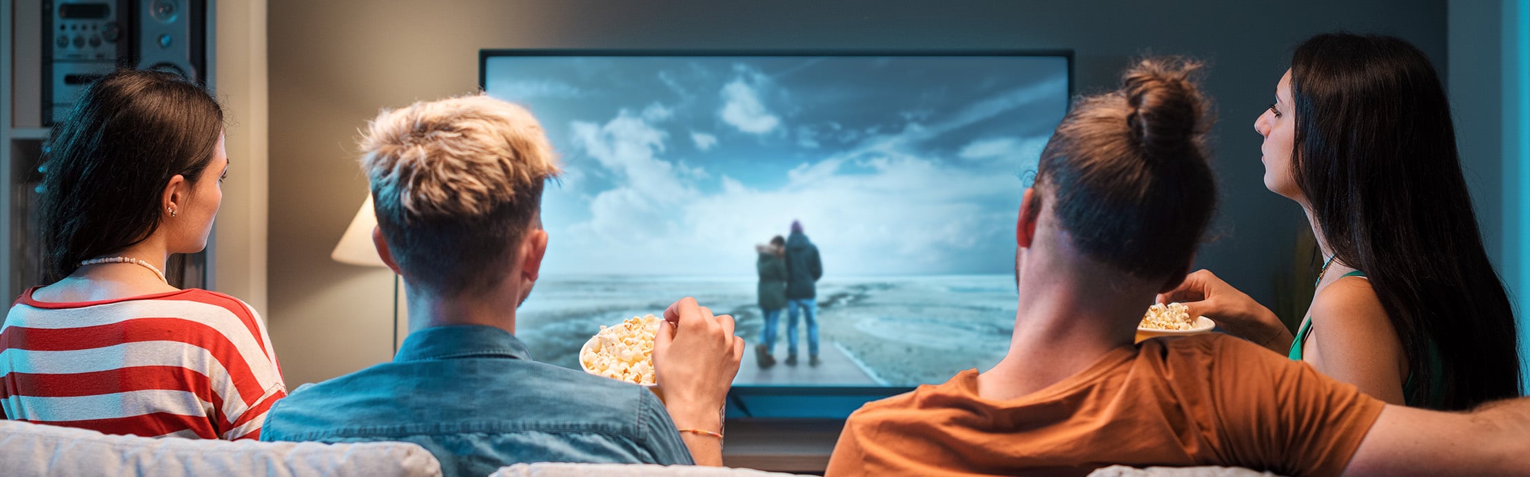 Vier Personen sitzen mit Popcorn auf einem Sofa und schauen gemeinsam einen Film im Fernsehen.