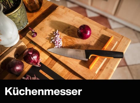 Ein Fiskars-Küchenmesser liegt neben fein gewürfelten roten Zwiebeln auf einem Holzschneidebrett in einer hellen Küche.